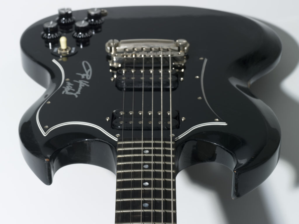 Electric guitar with black enamel-finish body and a dark brown timber neck. The body has two volume and two tone control knobs and a toggle switch. The guitar is viewed along the neck looking towards the body.